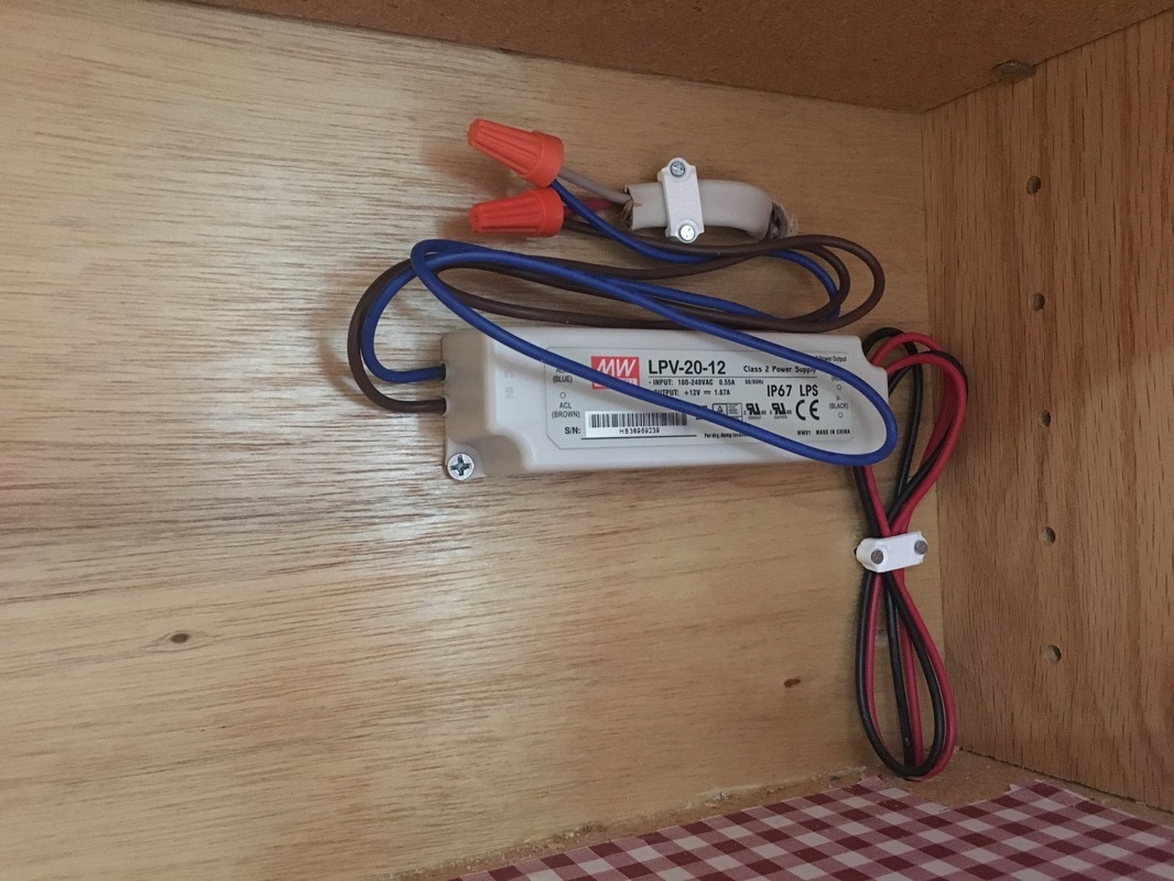 Uncovered electrical connection inside a kitchen cabinet.